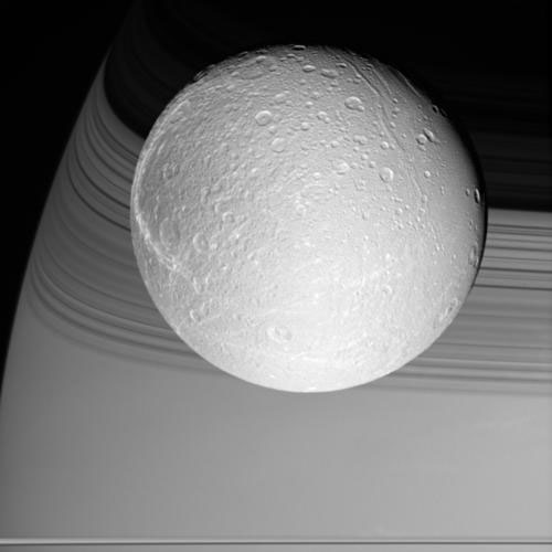 Спутник Сатурна Диона на фоне тени колец Сатурна, снятый широкоугольной камерой "Кассини" 9 октября 2005 года с расстояния в 1,8 миллиона километров. В нижней левой части диска можно заметить кратеры Дидо (Dido) и Антенор (Antenor). В кольцах выше видима темная "щель Кассини" между кольцами "A" и "B". Фото NASA/JPL/Space Science Institute с сайта saturn.jpl.nasa.gov